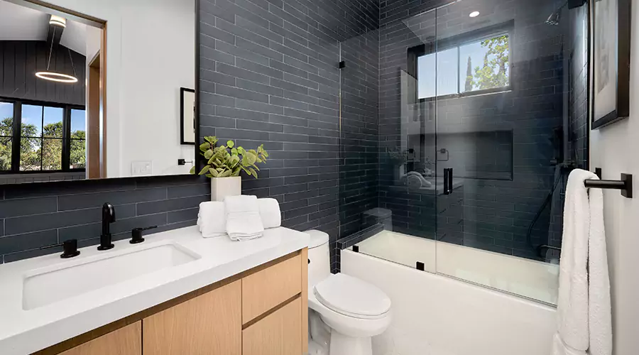 Bathroom remodel featuring a dark blue vanity, round wood mirror, and a tiled walk-in shower with sliding glass doors